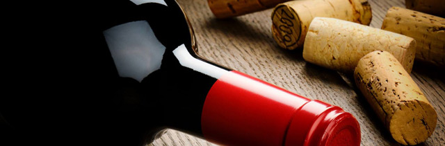 Close up of a wine bottle with dark red wine, posed with wine corks.